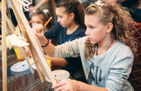 Children painting on canvases mounted on easels.