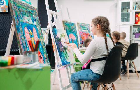 A child painting on a canvas while seated in a classroom.
