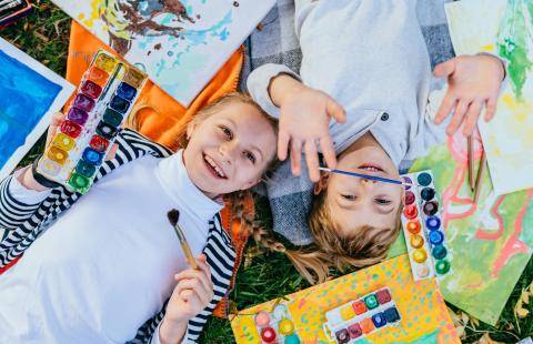 Children lying on the floor surrounded by watercolour paints and paper.